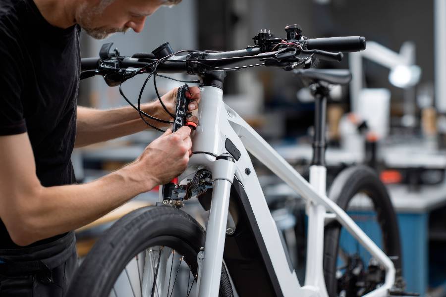 A close-up shot of a bicycle mechanic in a workshop carefully routing internal cables near the headtube and front fork of a modern white electric bike.