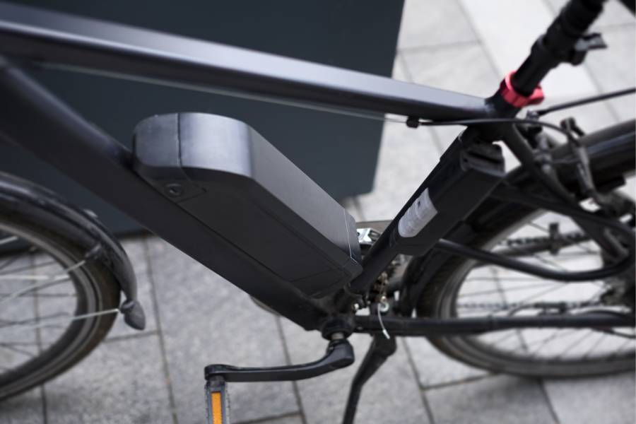 A close-up view of a dark grey electric bicycle frame highlighting its battery configuration. A large, black external battery pack is mounted on the downtube, while a smaller secondary battery or range extender is attached to the seat tube.
